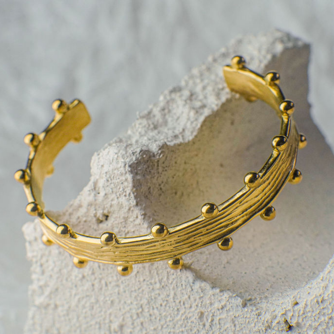 Gold bracelet with bead detailing on a textured stone surface