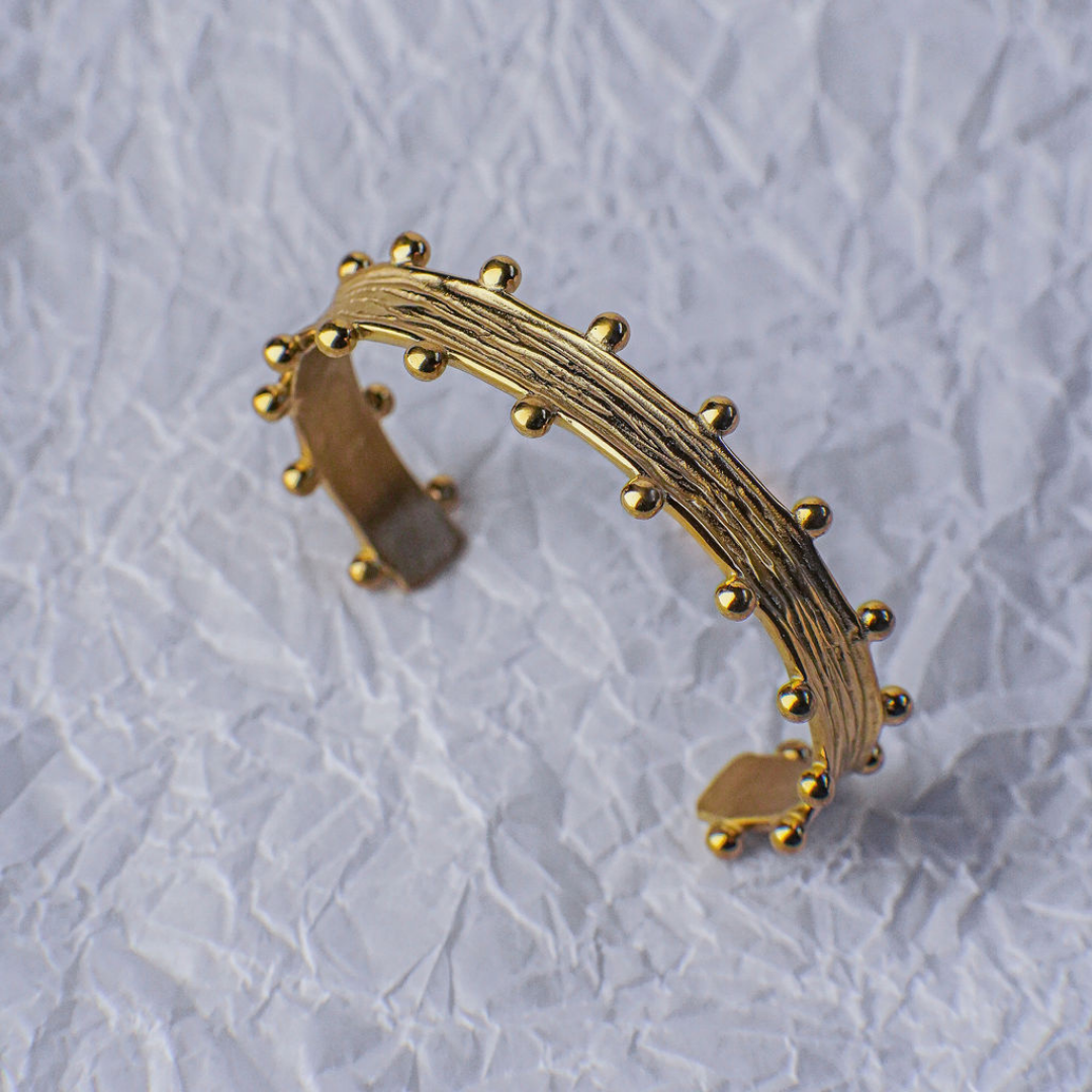 Gold bracelet with textured design on a light gray background