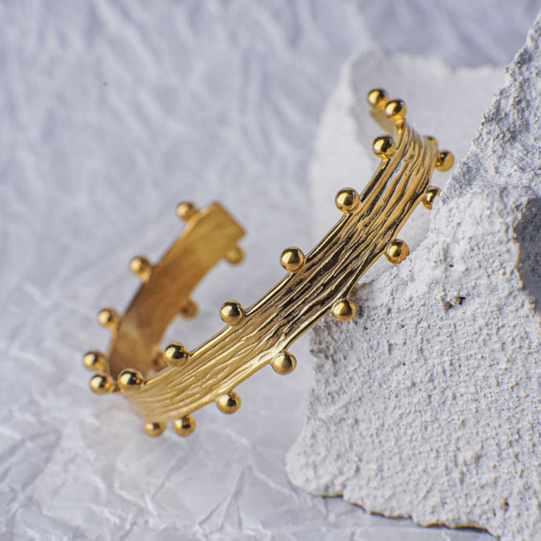 Gold bracelet with bead detailing on a textured stone surface