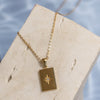 A gold-colored necklace with a rectangular pendant featuring a star design, displayed on a textured white surface.