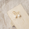 Pearl earrings on a beige stone surface