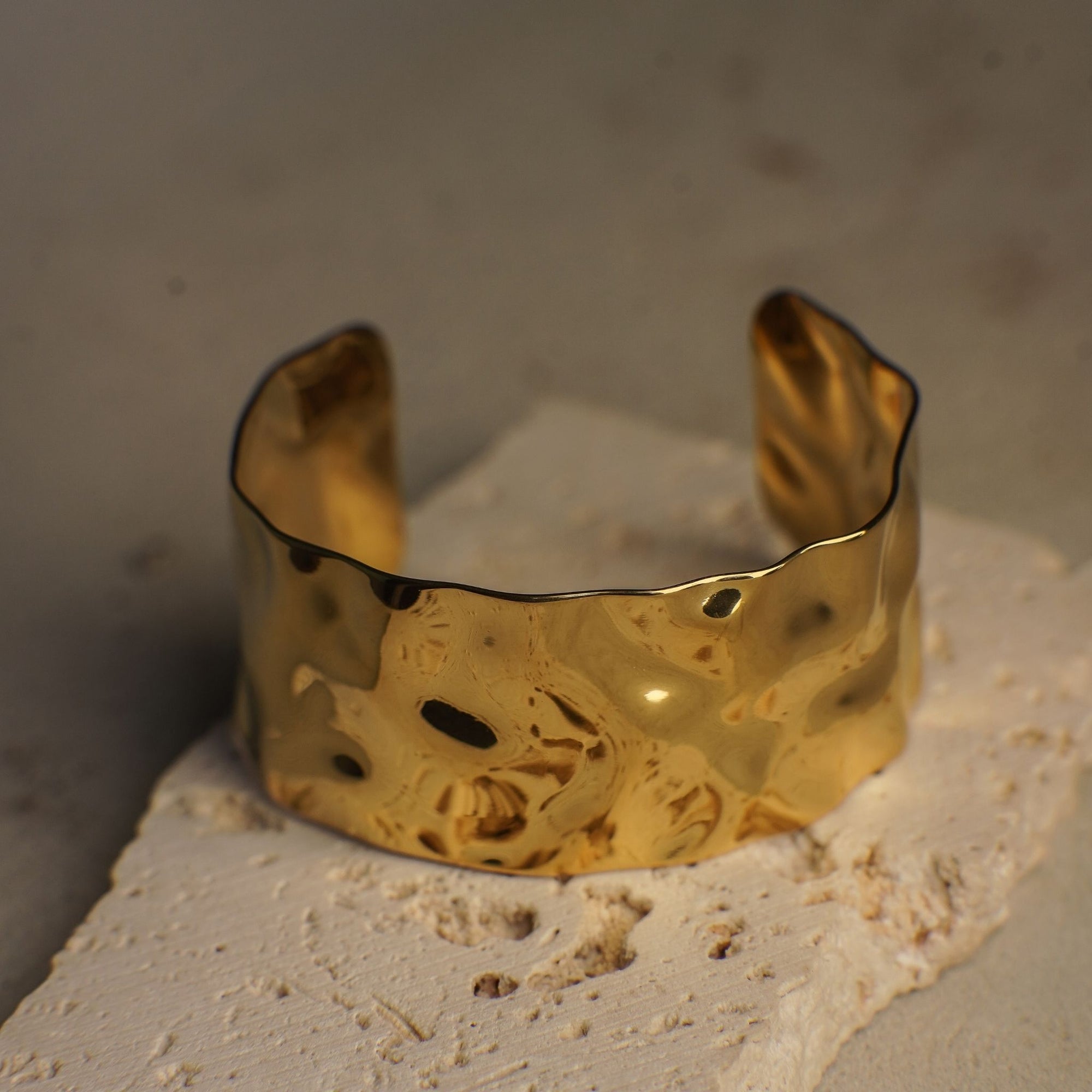 Gold cuff bracelet on a textured surface with a neutral background