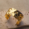 Gold ring with a marbled design on a textured beige surface
