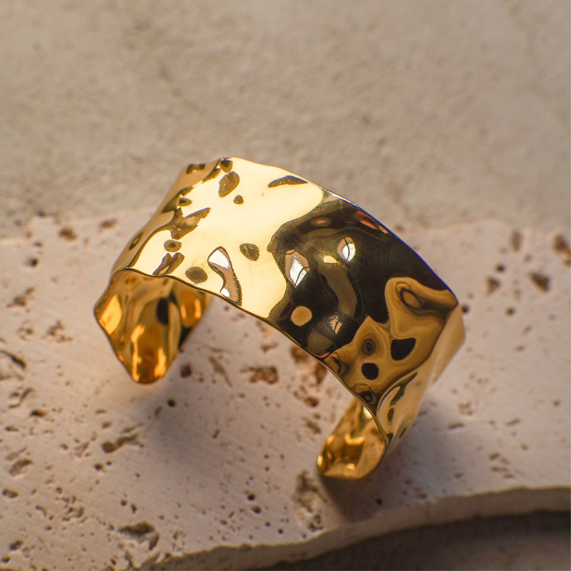 Gold ring with a marbled design on a textured beige surface