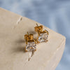 A pair of gold earrings with zirconia on a textured surface