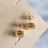 Two gold earrings with zirconia on a textured surface