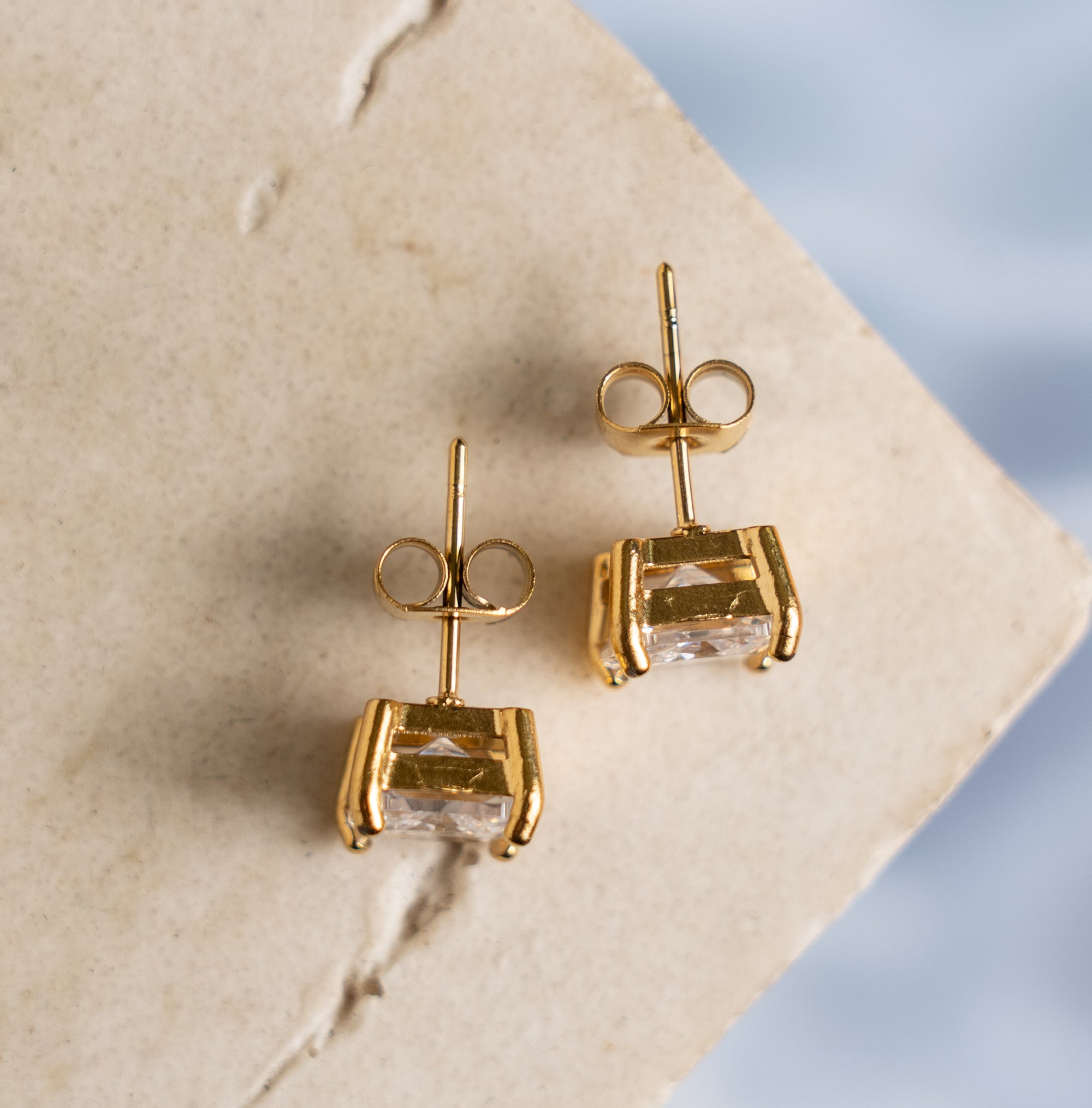 Two gold earrings with zirconia on a textured surface