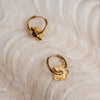 A pair of gold-colored hoop earrings with a star design, displayed on a textured surface.