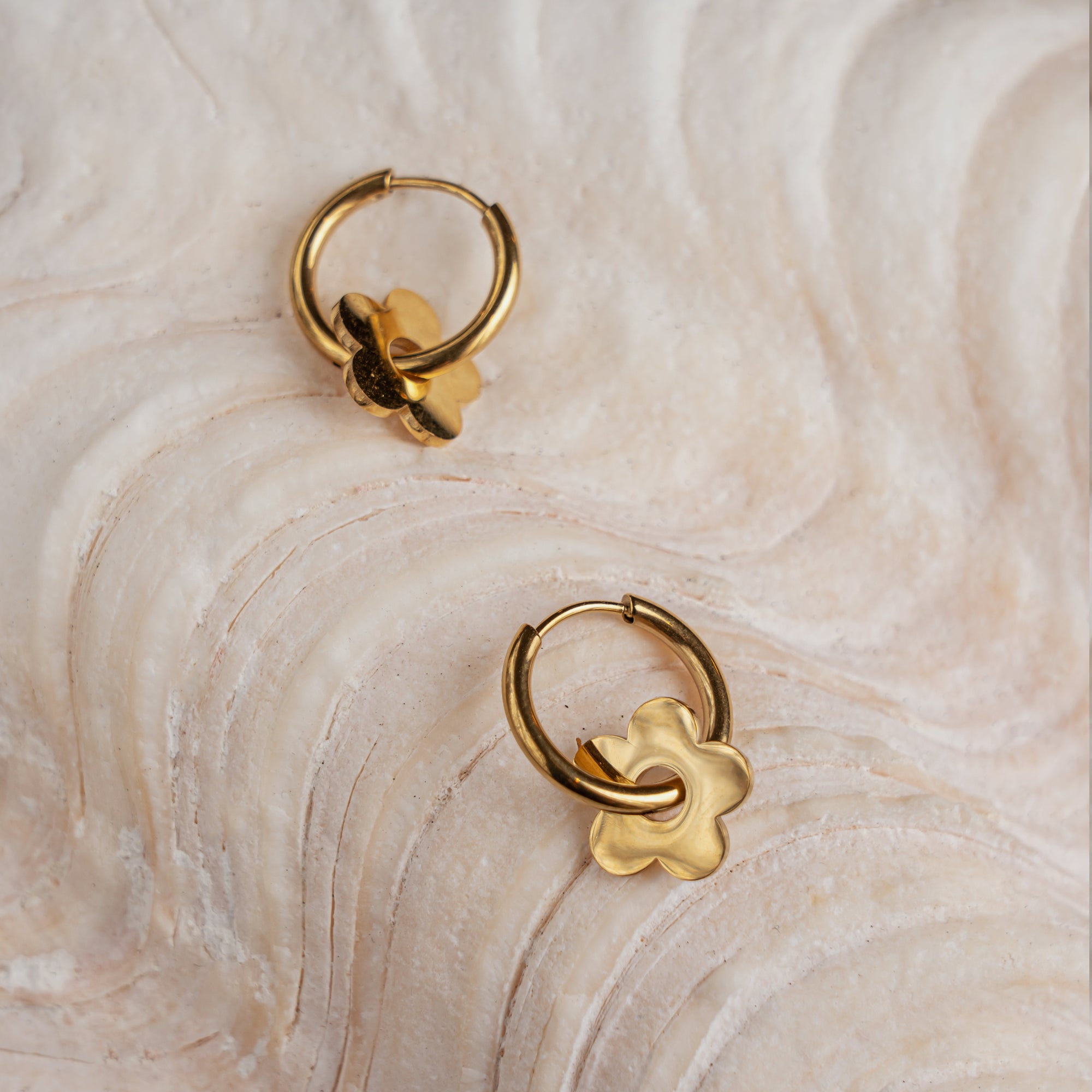 A pair of gold-colored hoop earrings with a star design, displayed on a textured surface.