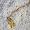 Gold necklace with a detailed pendant on a sandy surface