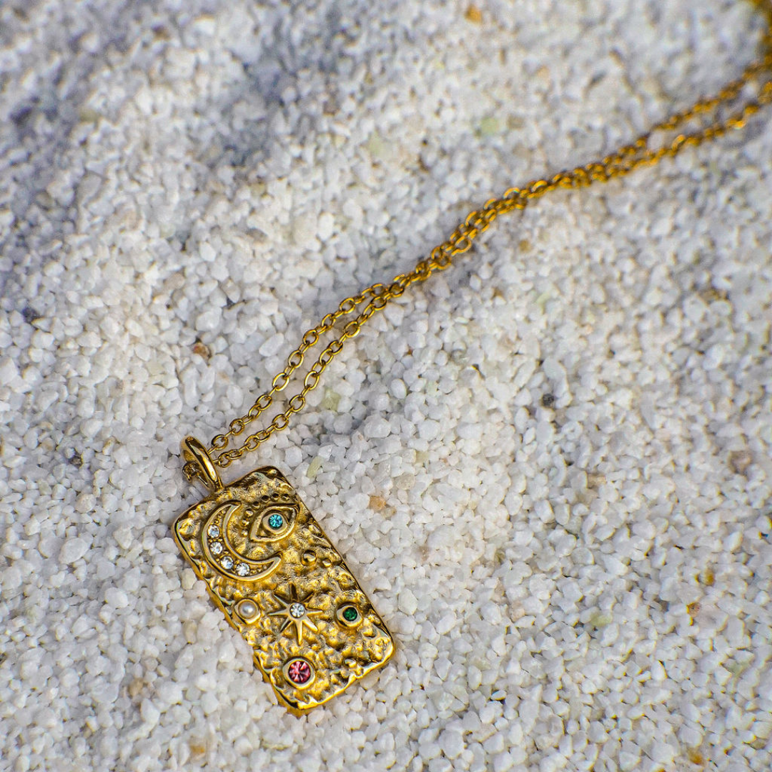 Gold necklace with a detailed pendant on a sandy surface