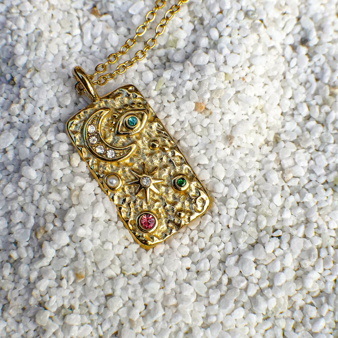 Gold pendant necklace with gemstones on a sandy background
