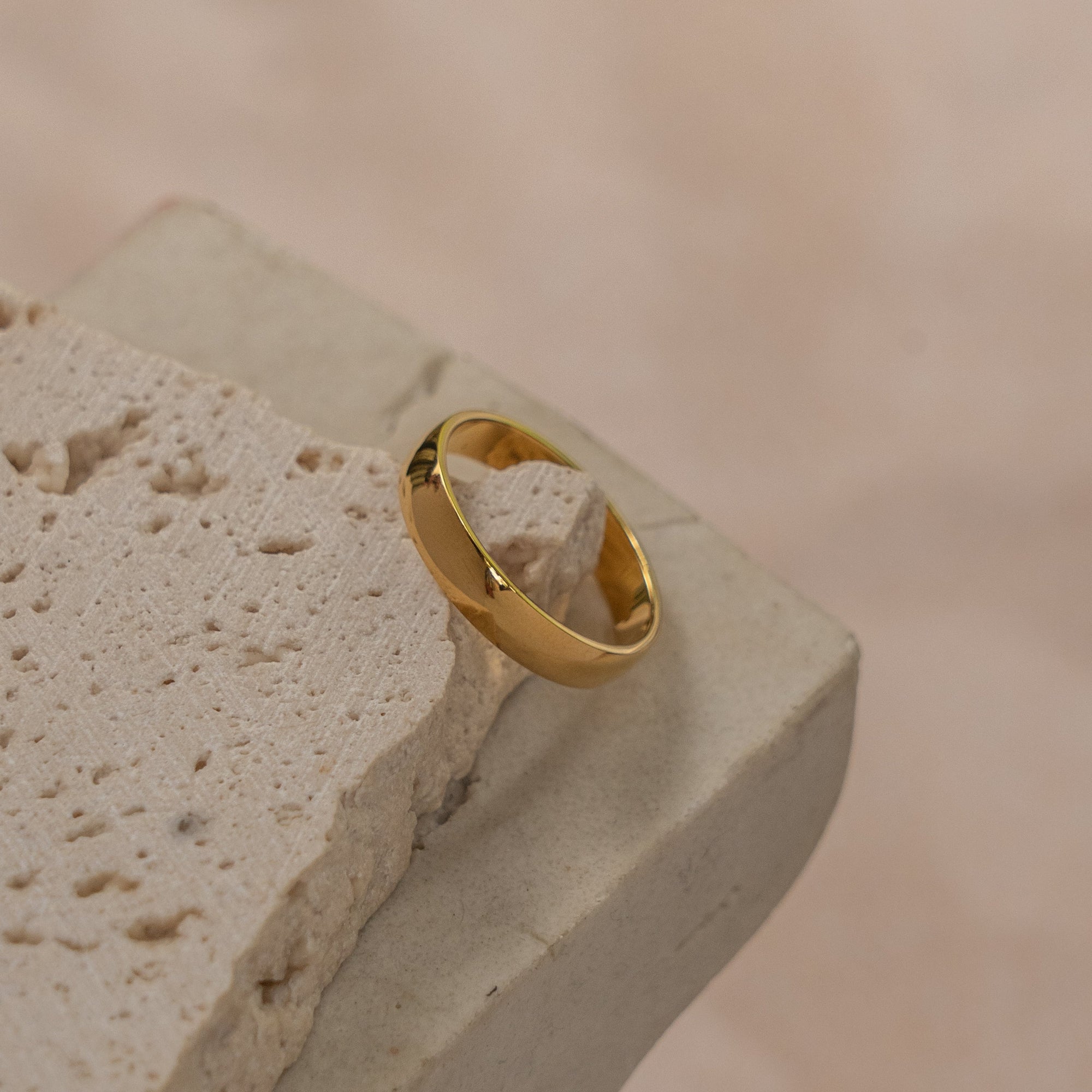 A gold-colored ring placed on a textured stone surface.