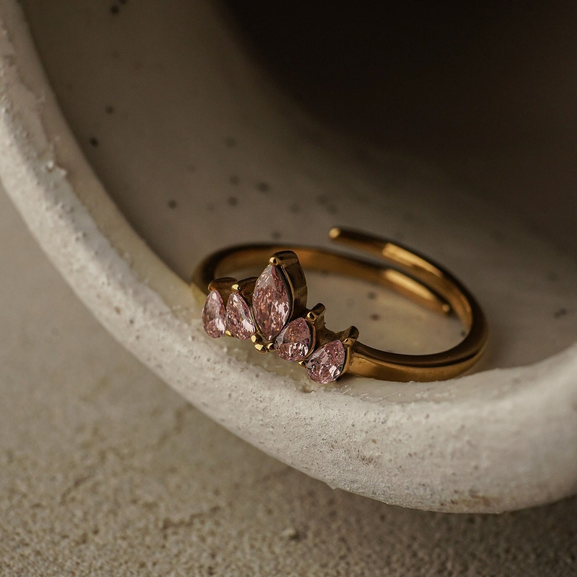 Gold ring with pink gemstones on a textured surface