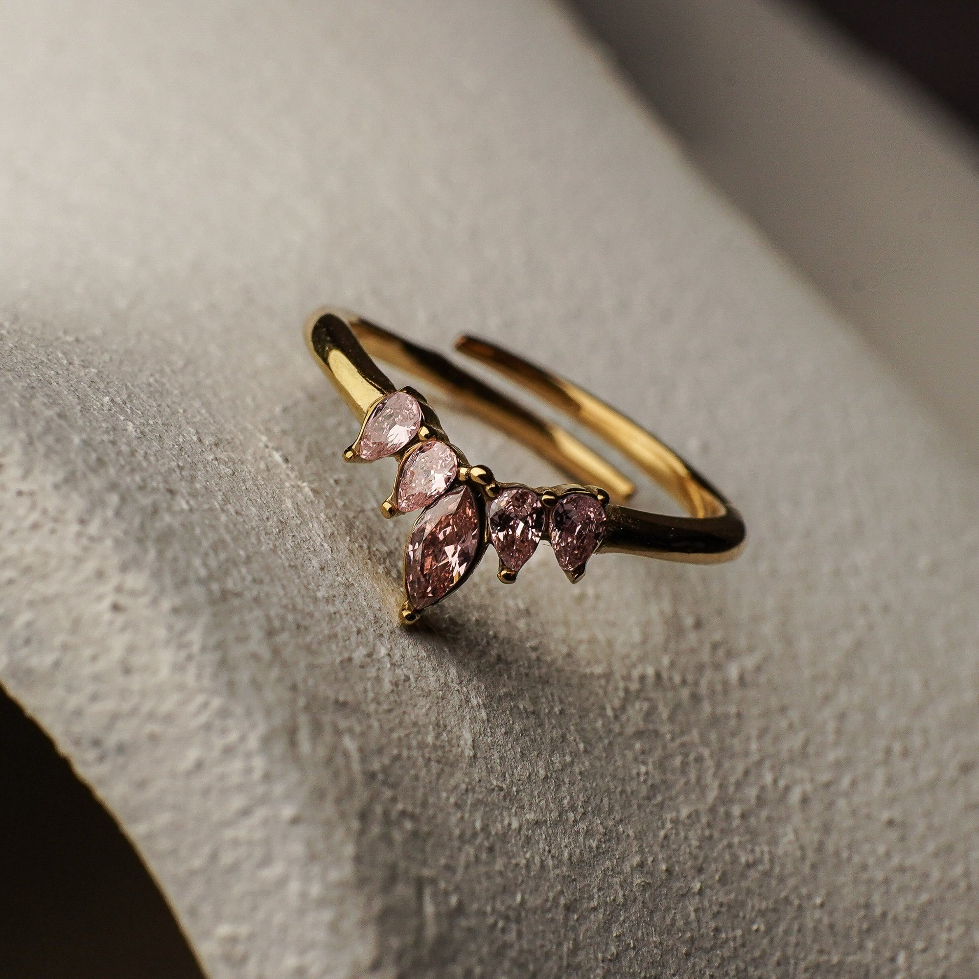 Gold ring with pink gemstones on a textured surface