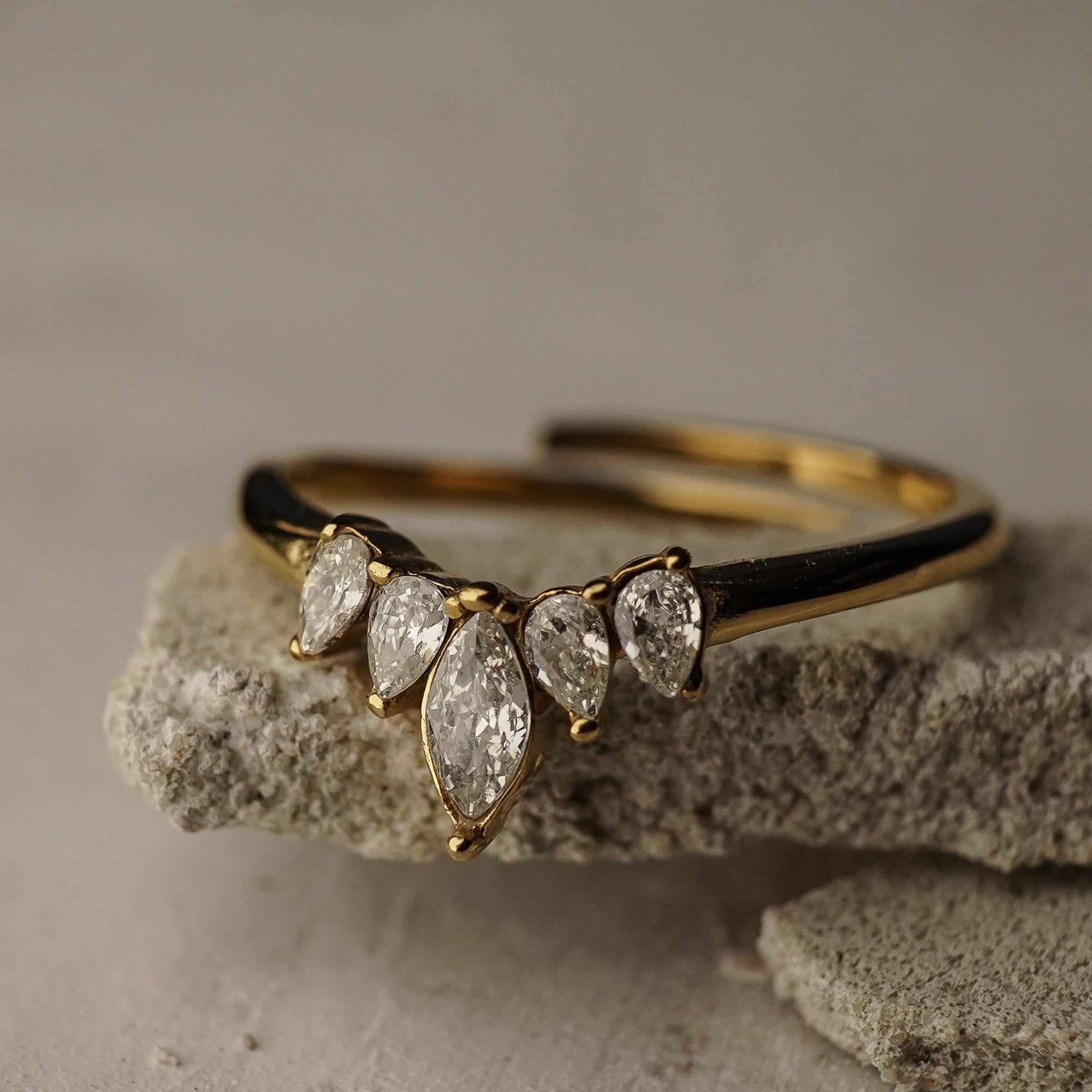 Gold ring with teardrop-shaped diamonds on a textured stone surface