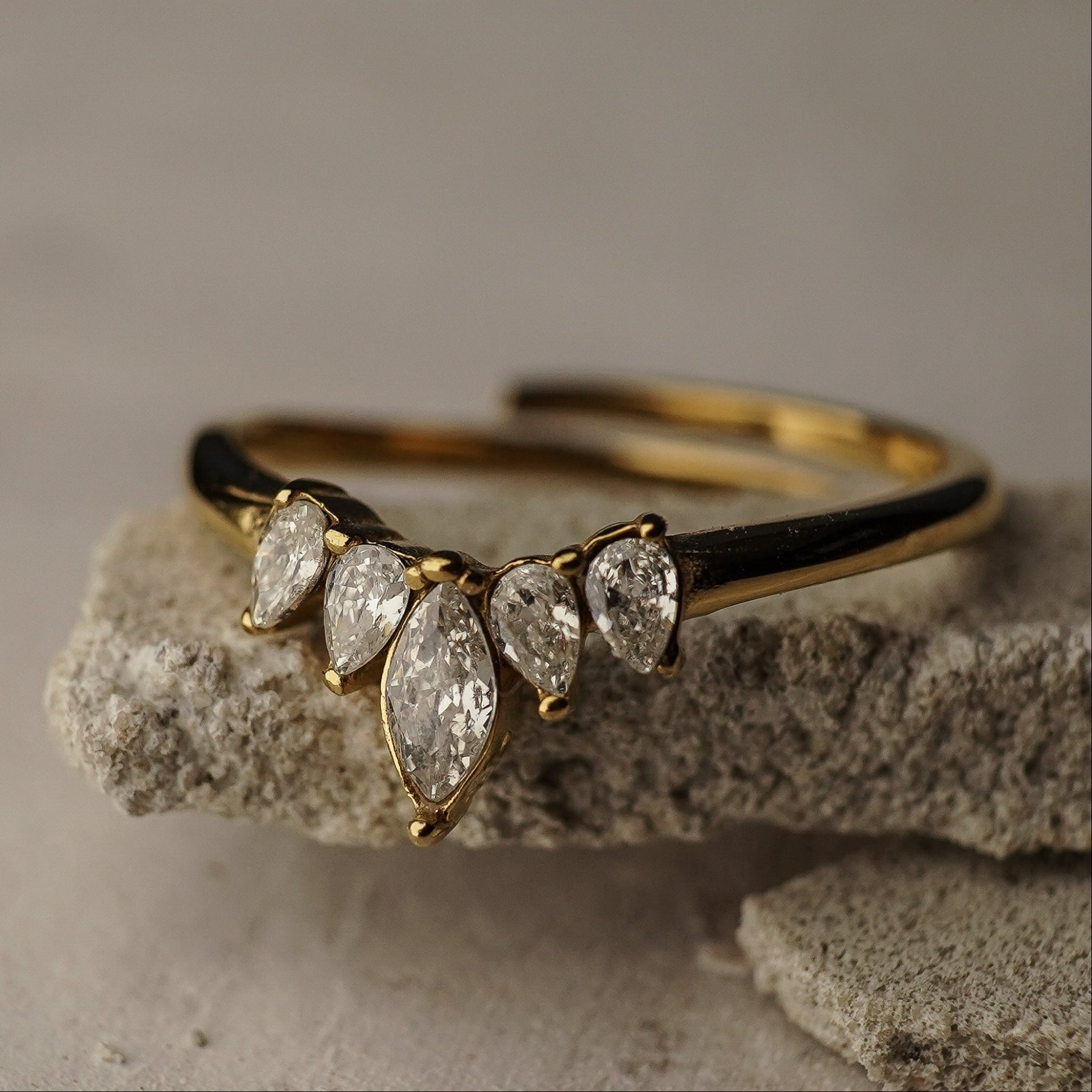 Gold ring with teardrop-shaped diamonds on a textured stone surface