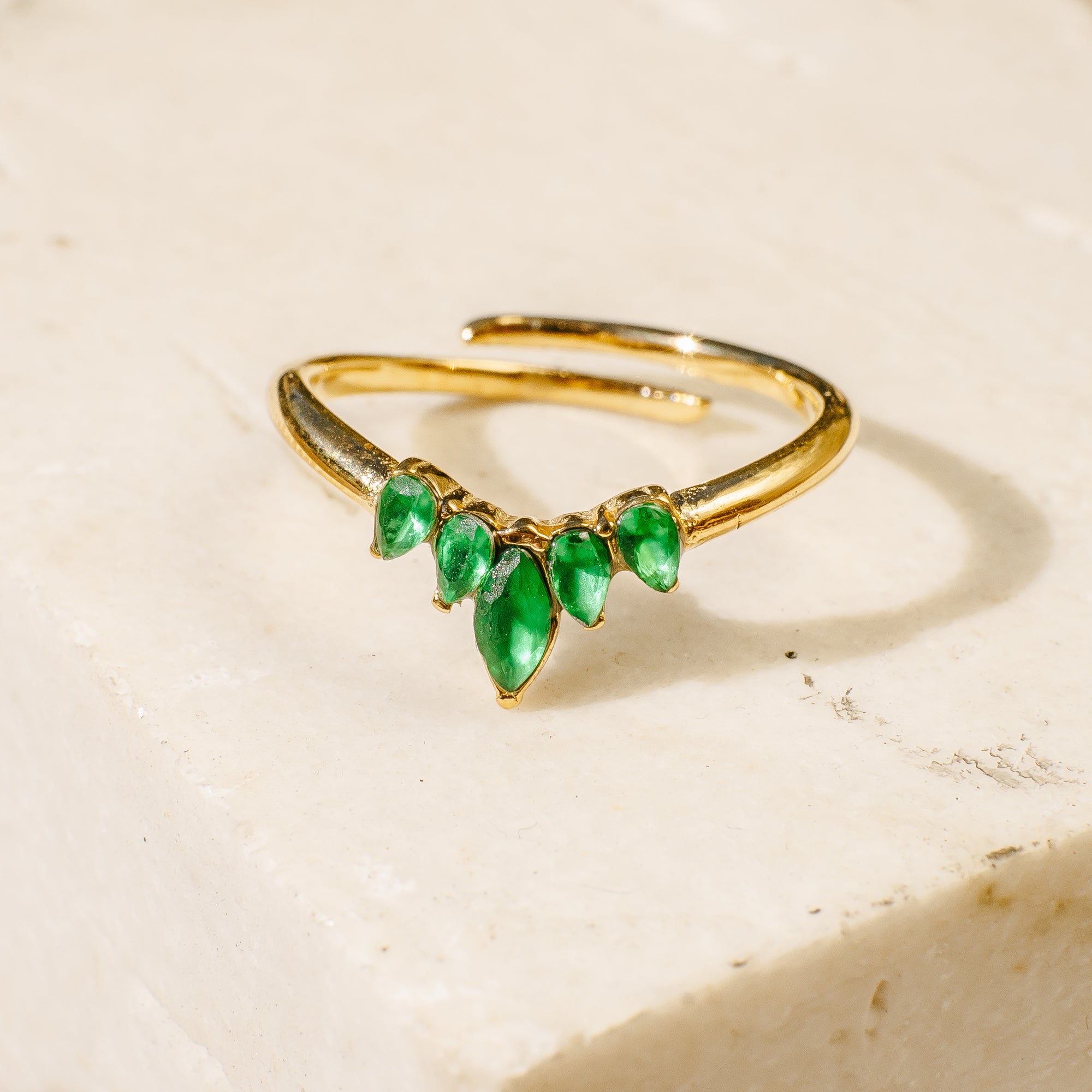 Gold ring with green gemstones on a beige background