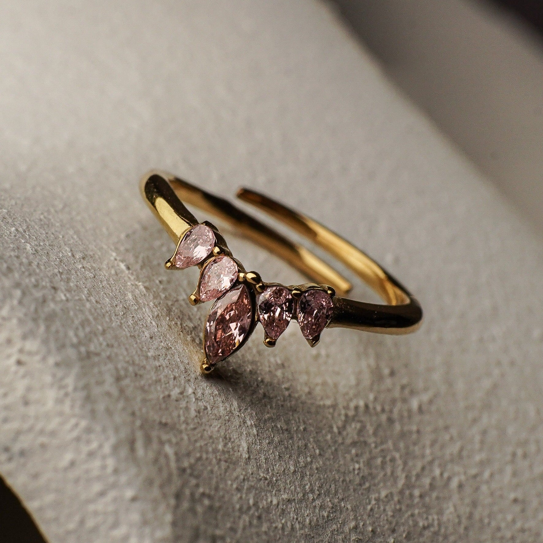 Gold ring with pink gemstones on a textured surface