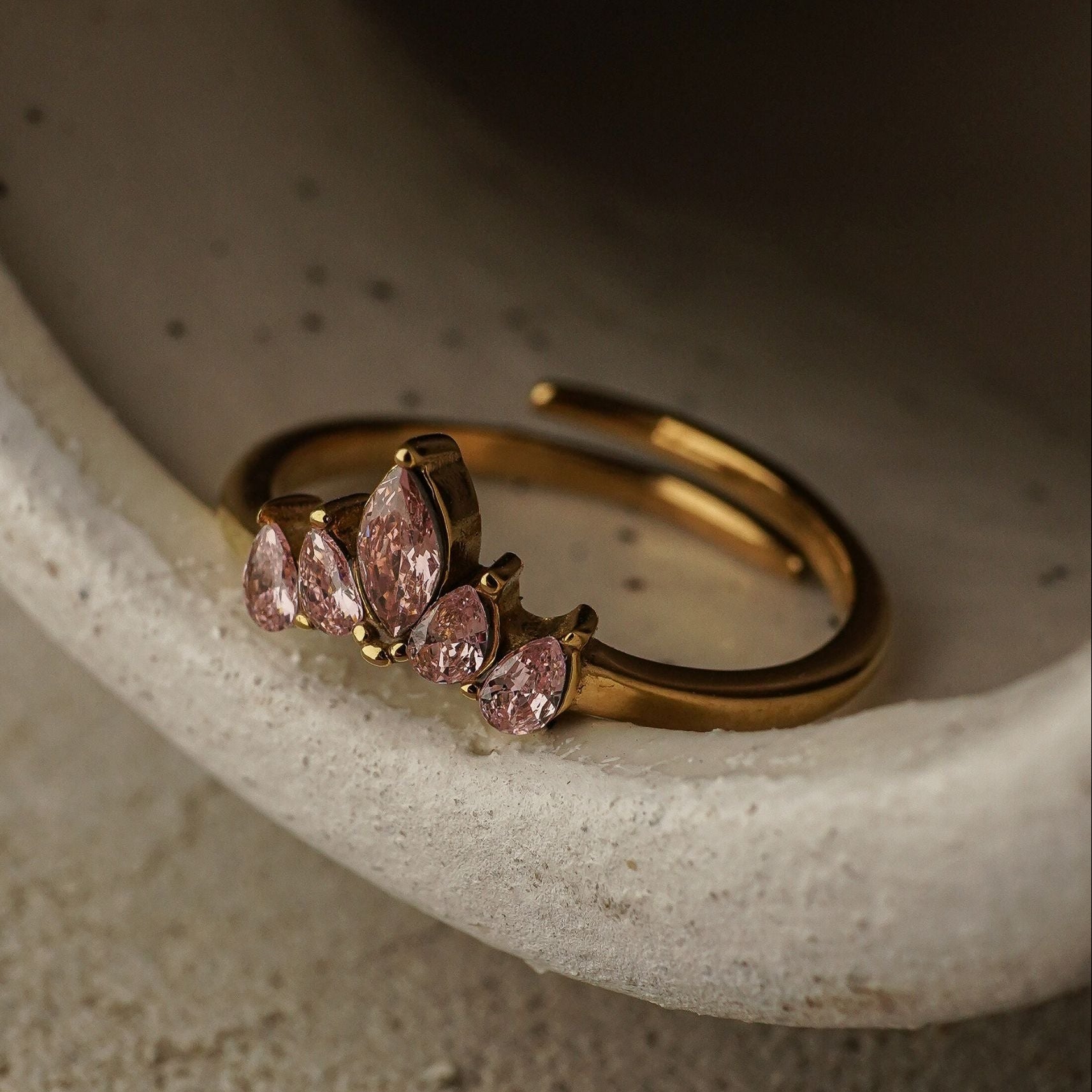 Gold ring with pink gemstones on a textured surface