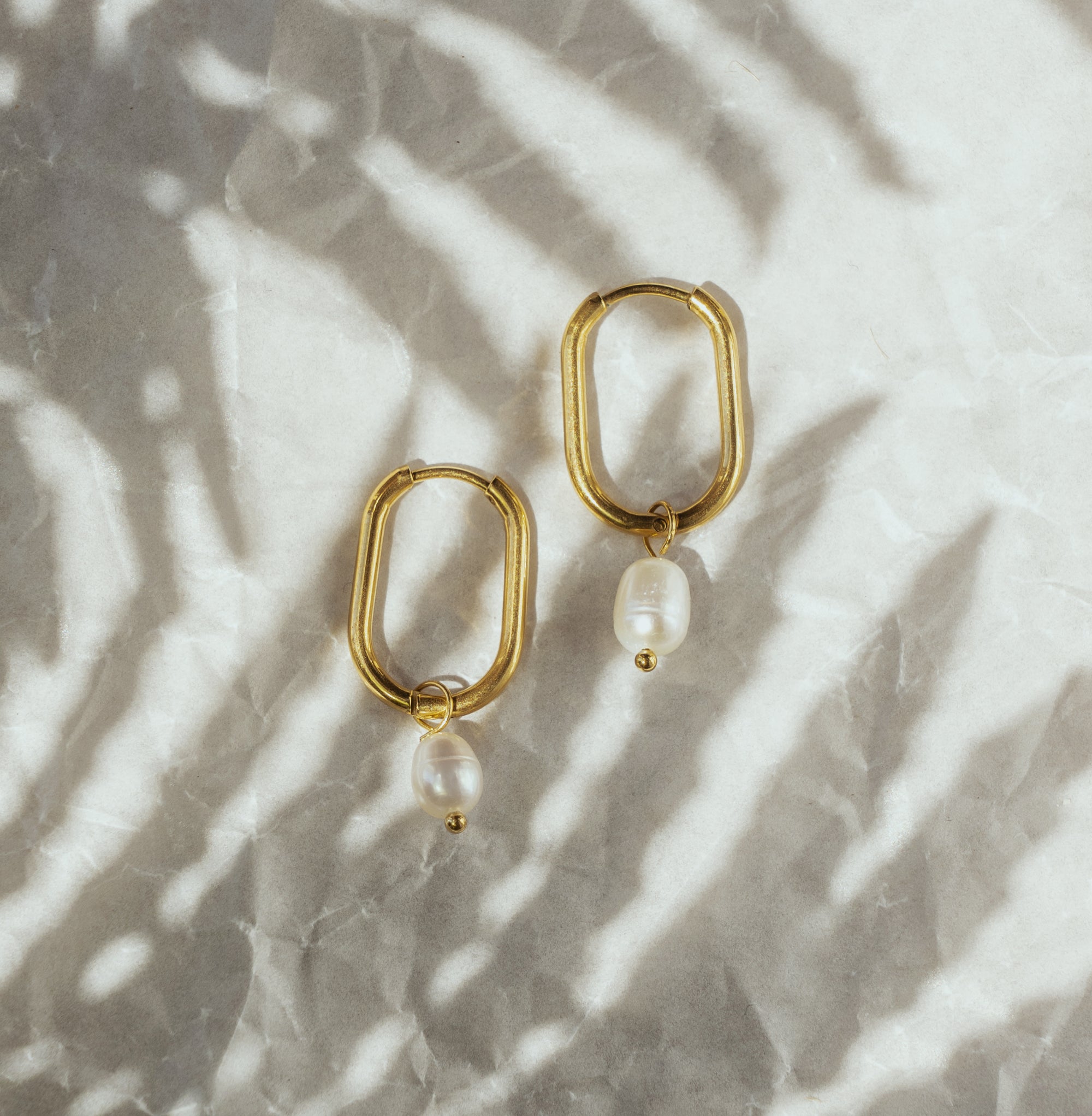 A pair of gold-colored hoop earrings with white pearls attached to them, displayed on a textured surface.