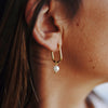 A woman wearing Mara Gold Pearl Earrings