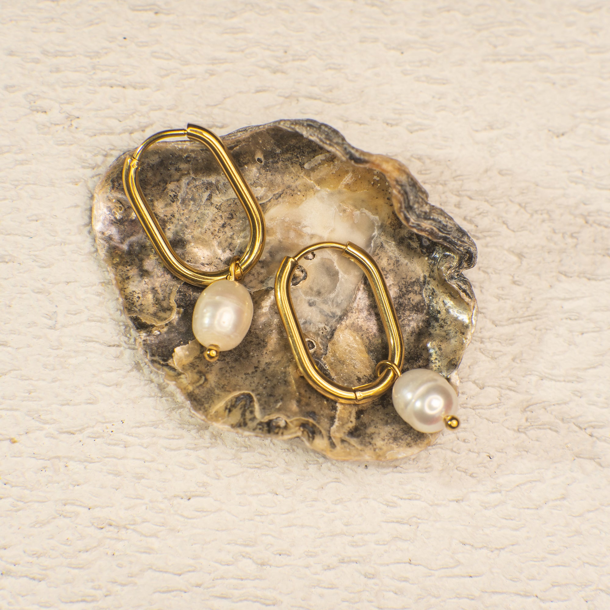 Gold hoop earrings with pearls on a textured beige background