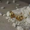 Gold earrings on a textured surface with pebbles