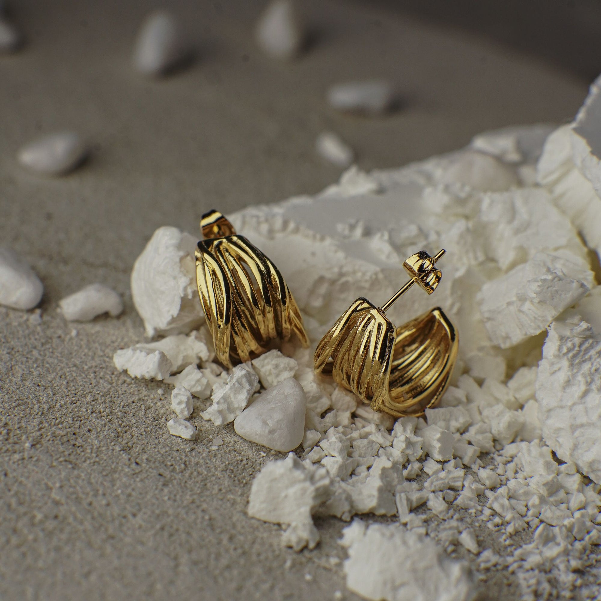 Gold earrings on a textured surface with pebbles
