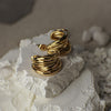 Gold hoop earrings on a textured white surface with a blurred natural background