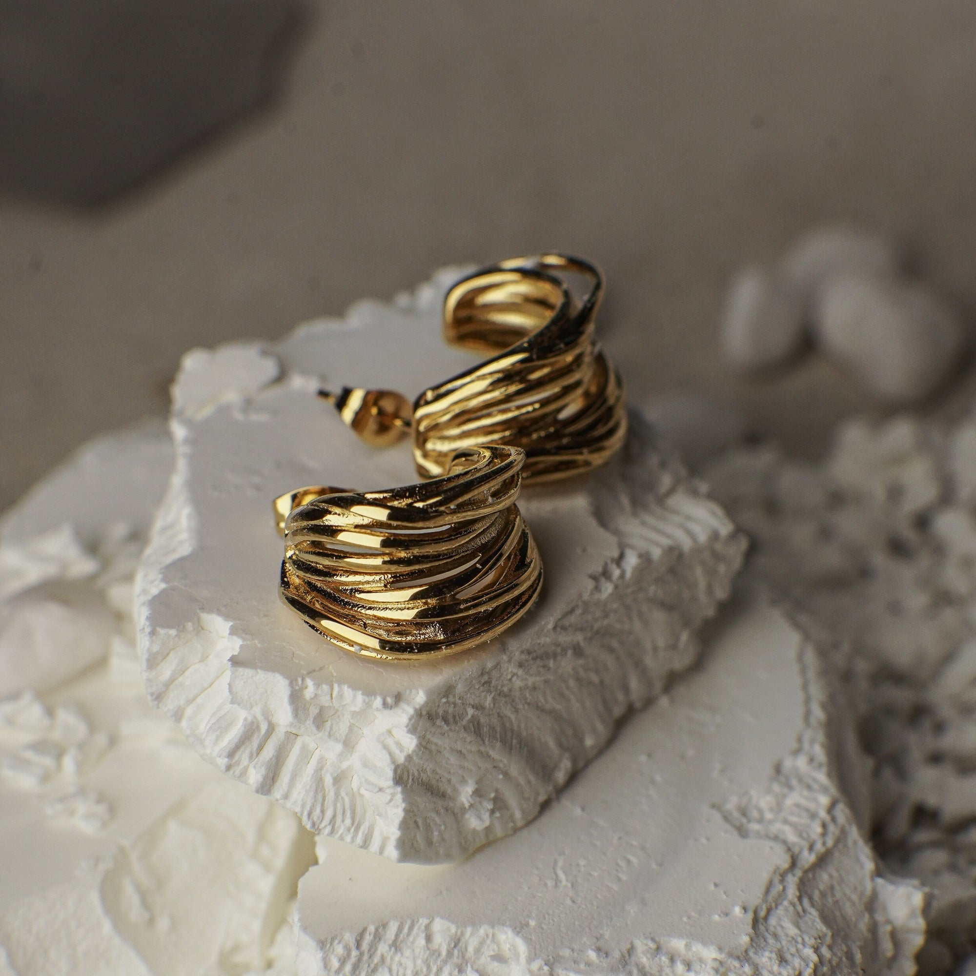 Gold hoop earrings on a textured white surface with a blurred natural background