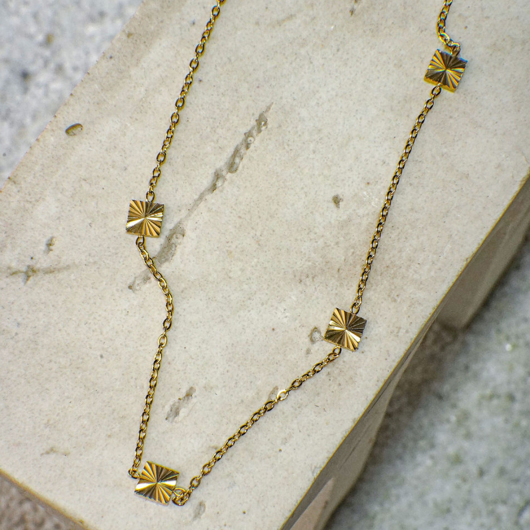 Gold necklace with geometric pendants on a textured surface