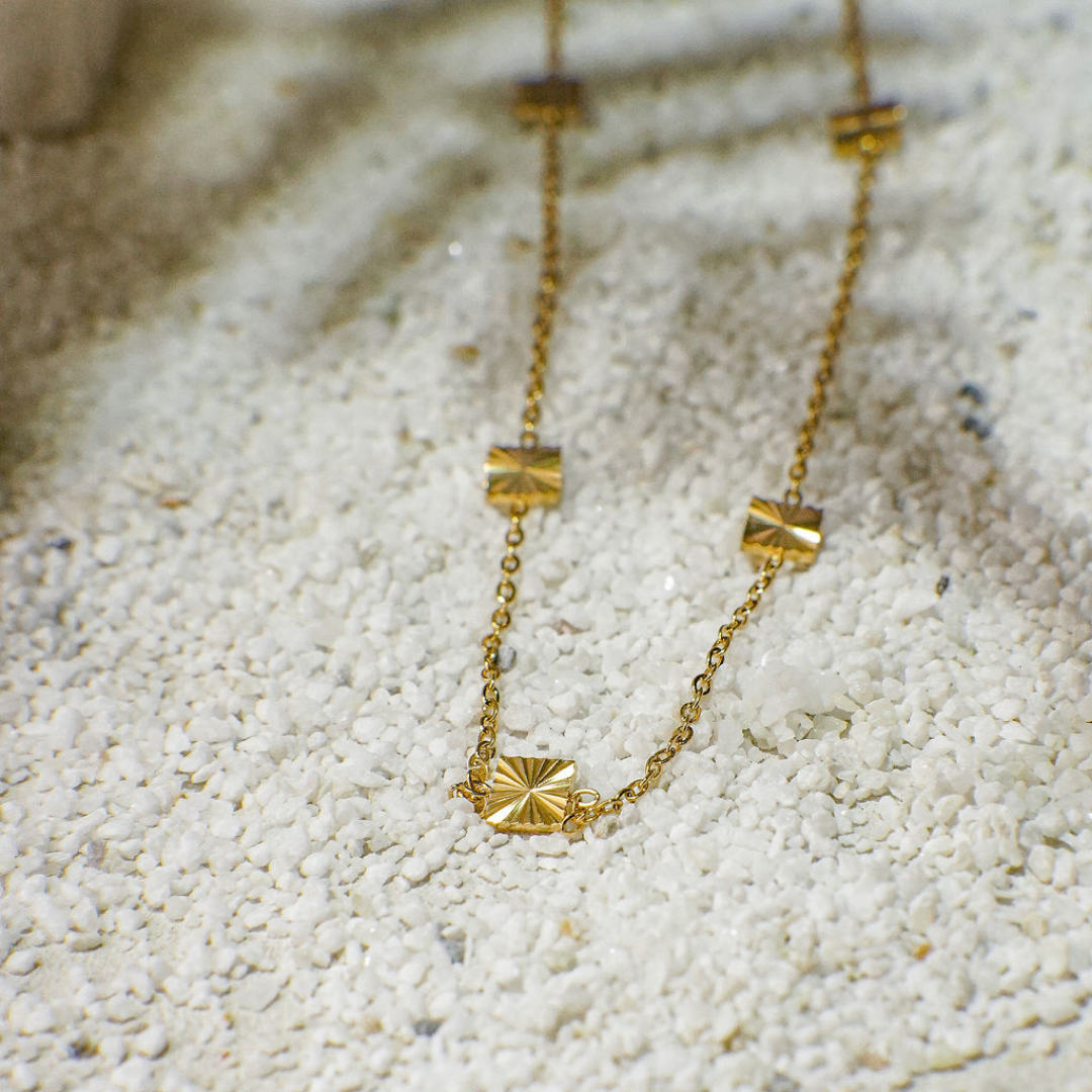 Gold necklace with geometric pendants on a textured white surface