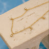 Gold necklace with small diamond-like pendants on a beige stone surface.
