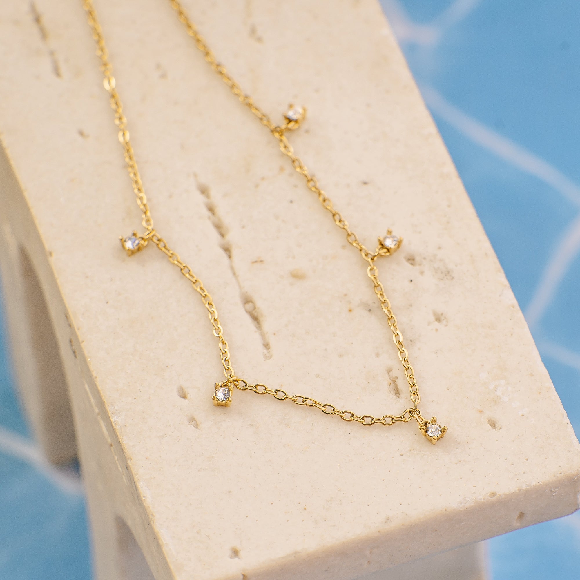 Gold necklace on a white stand with a blue tiled background