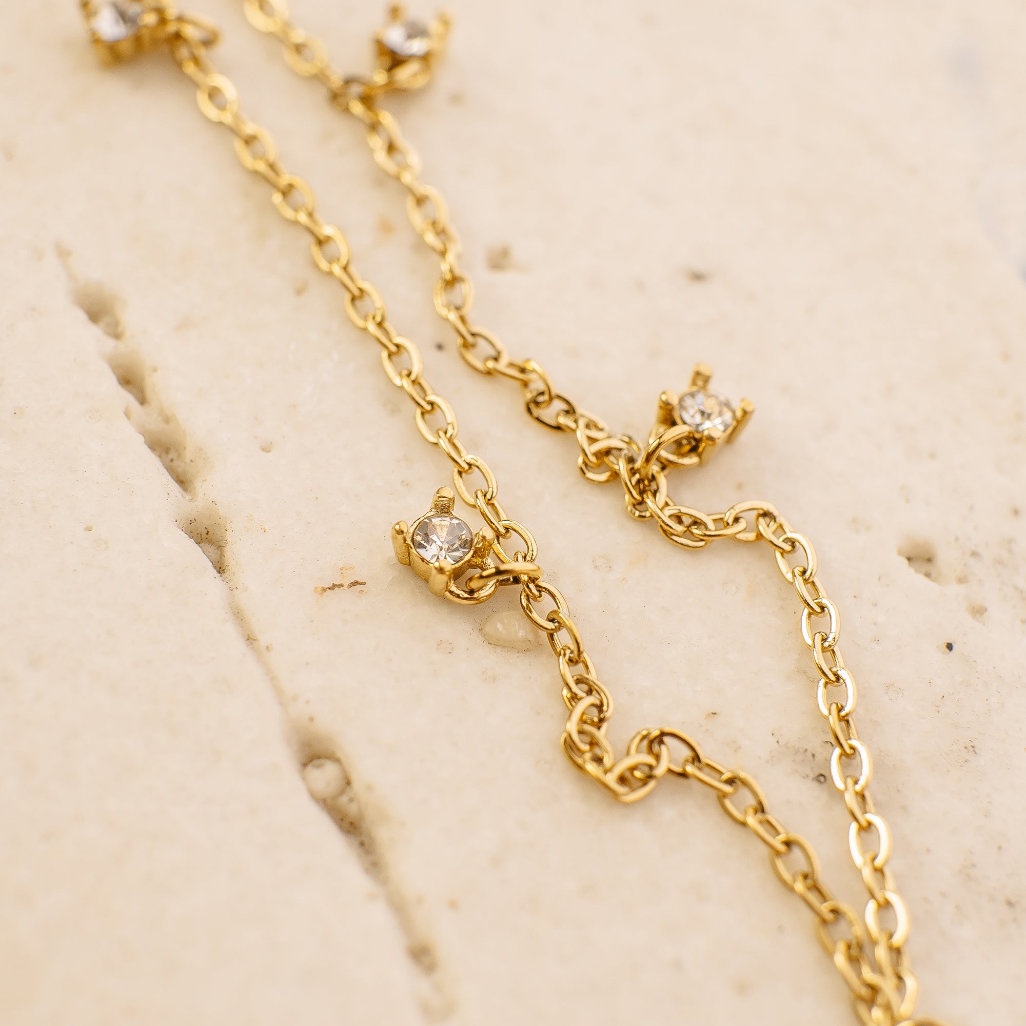 Gold chain necklace with small diamond-like stones on a beige marble surface