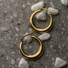 Gold hoop earrings on a textured surface with small stones.