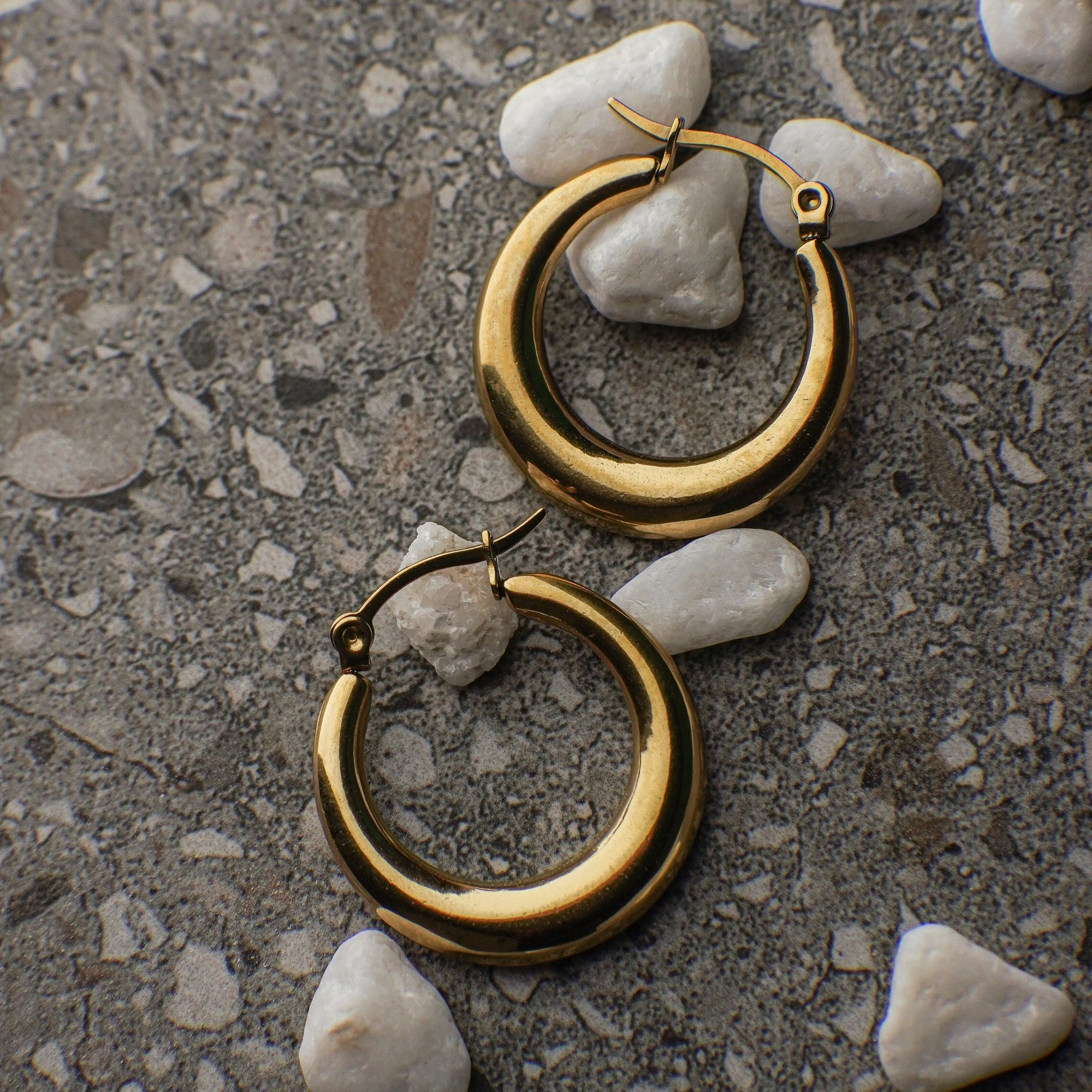 Gold hoop earrings on a textured surface with small stones.