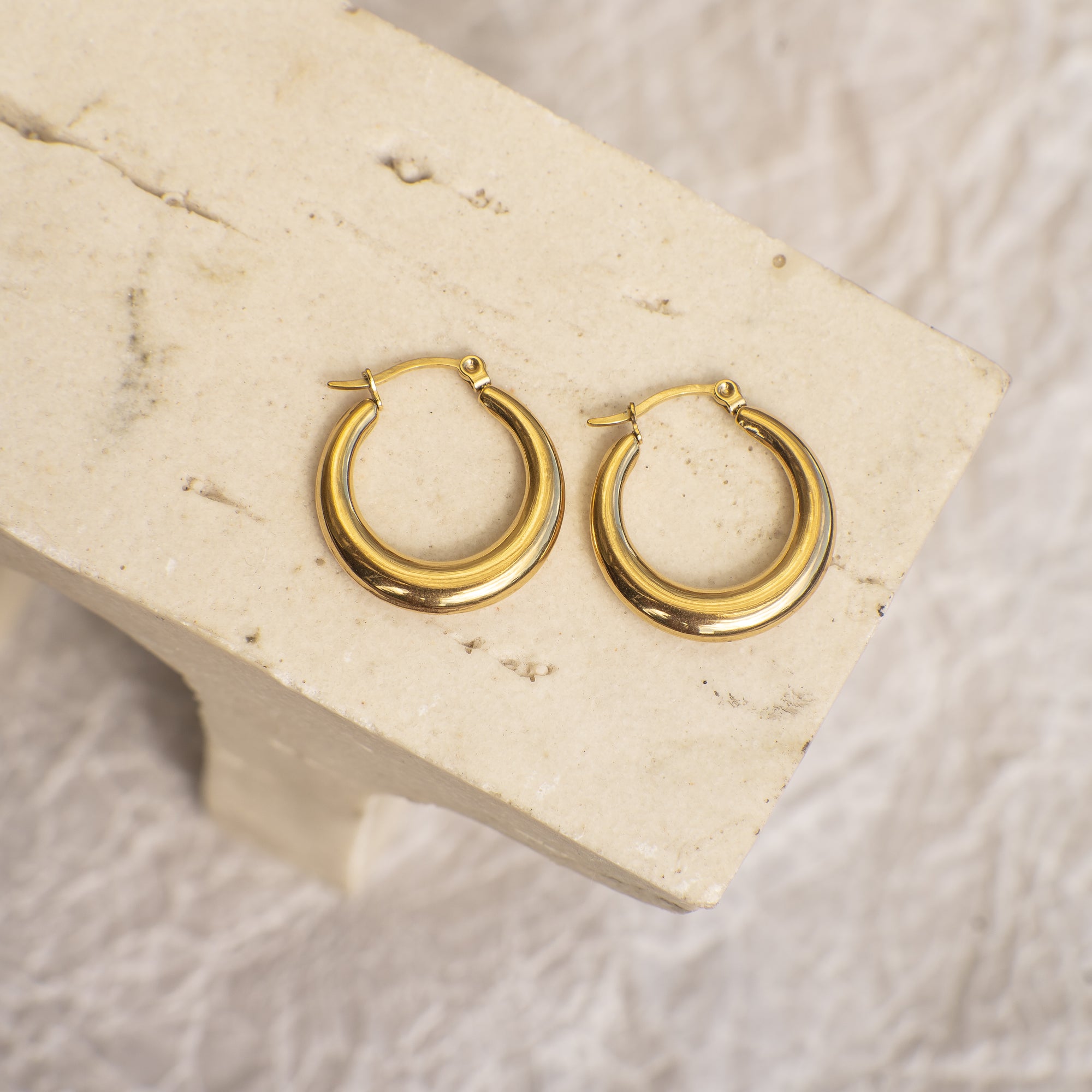 Gold hoop earrings on a beige stone surface