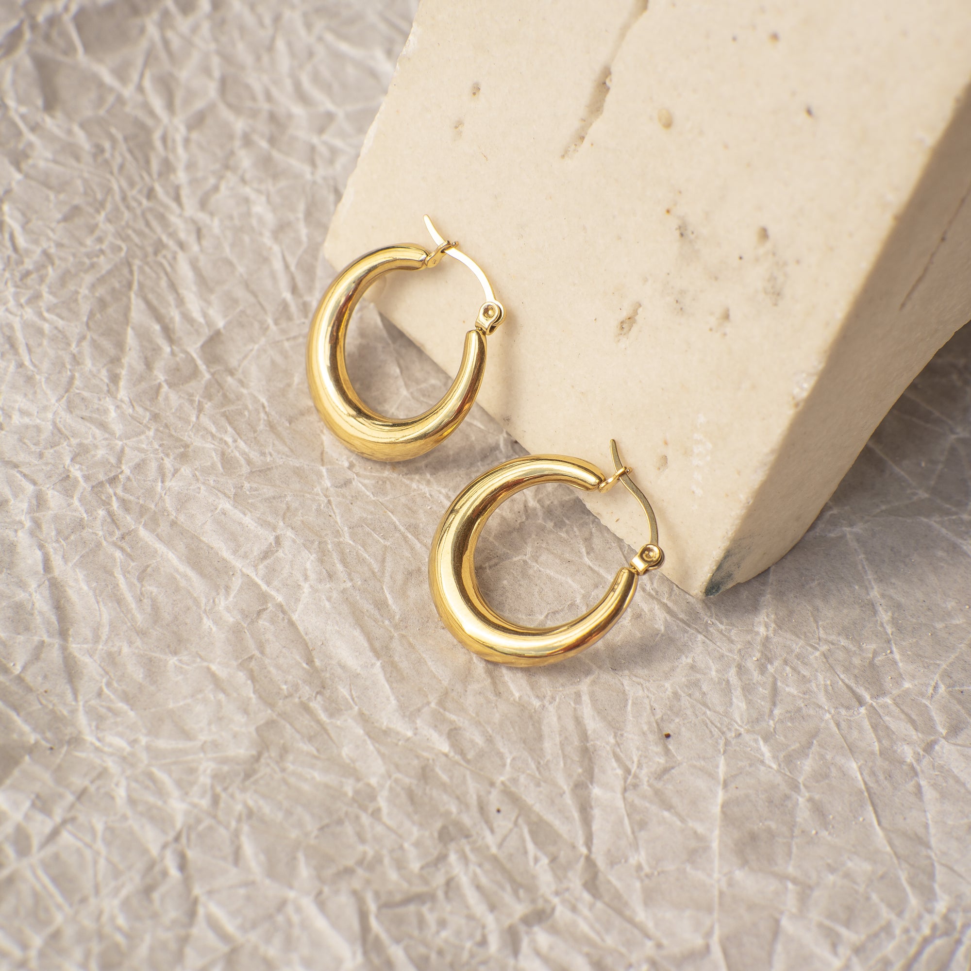 Gold hoop earrings on a textured stone surface