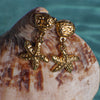 Gold starfish earrings on a shell with a blurred natural background
