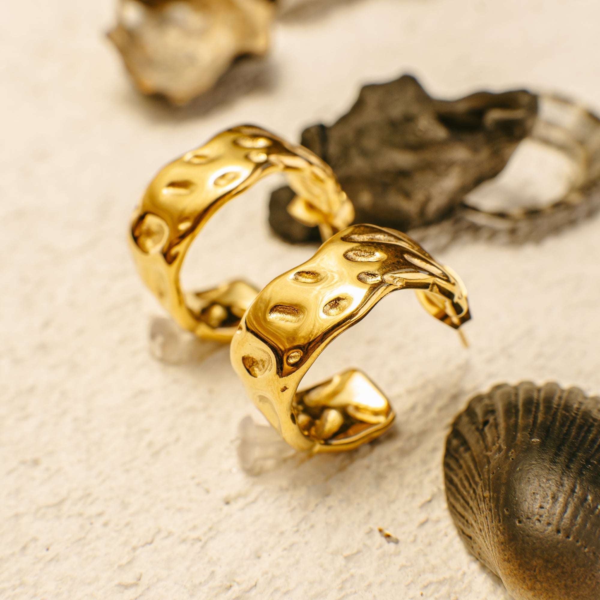 Gold hoop earrings on a textured beige surface with natural elements.