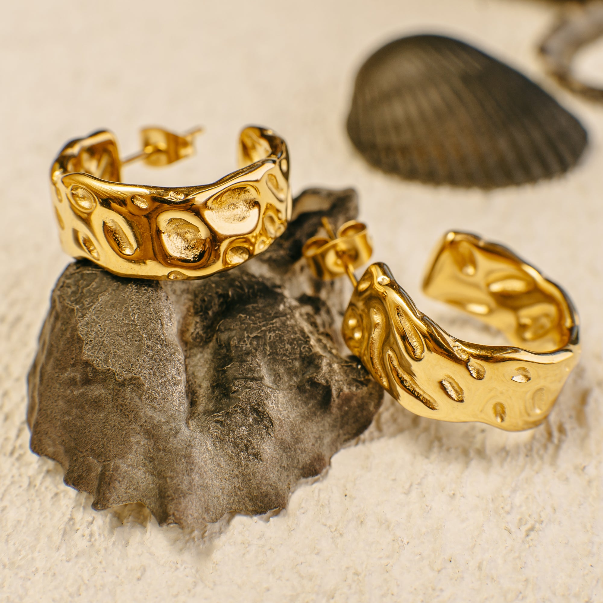Gold hoop earrings on a rock with a shell in the background