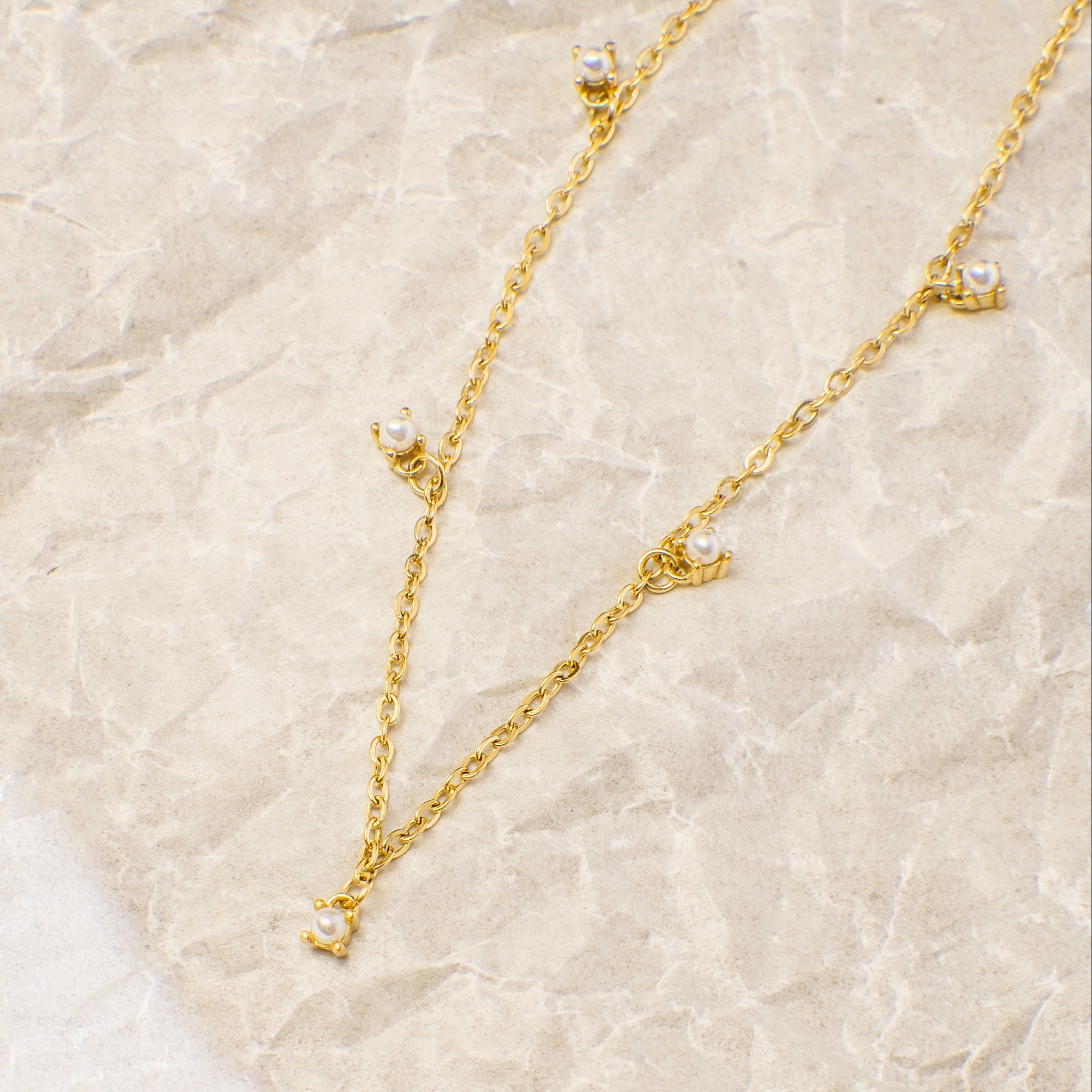 Gold necklace and earrings on a beige marble surface