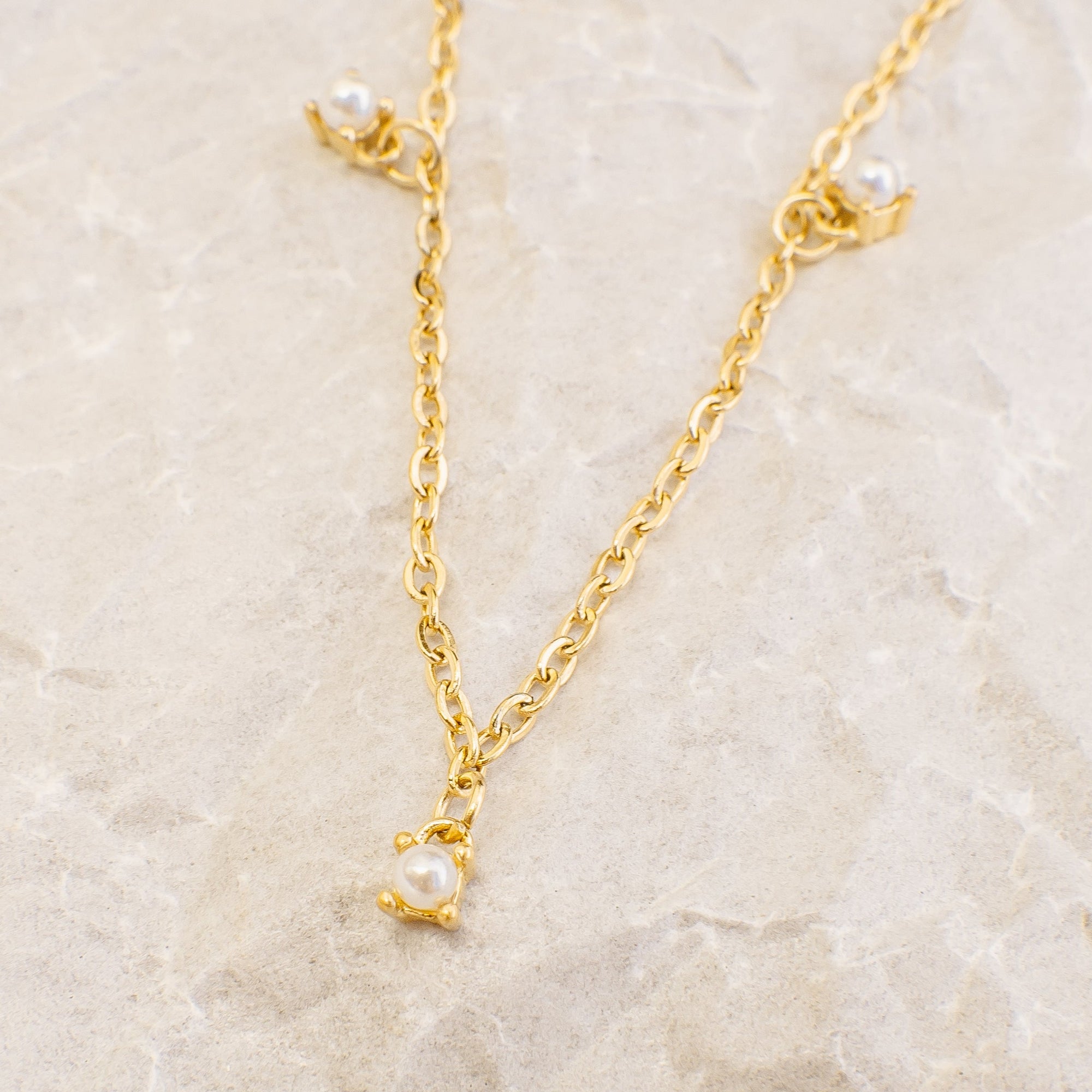 Gold necklace with pearl pendants on a beige marble background