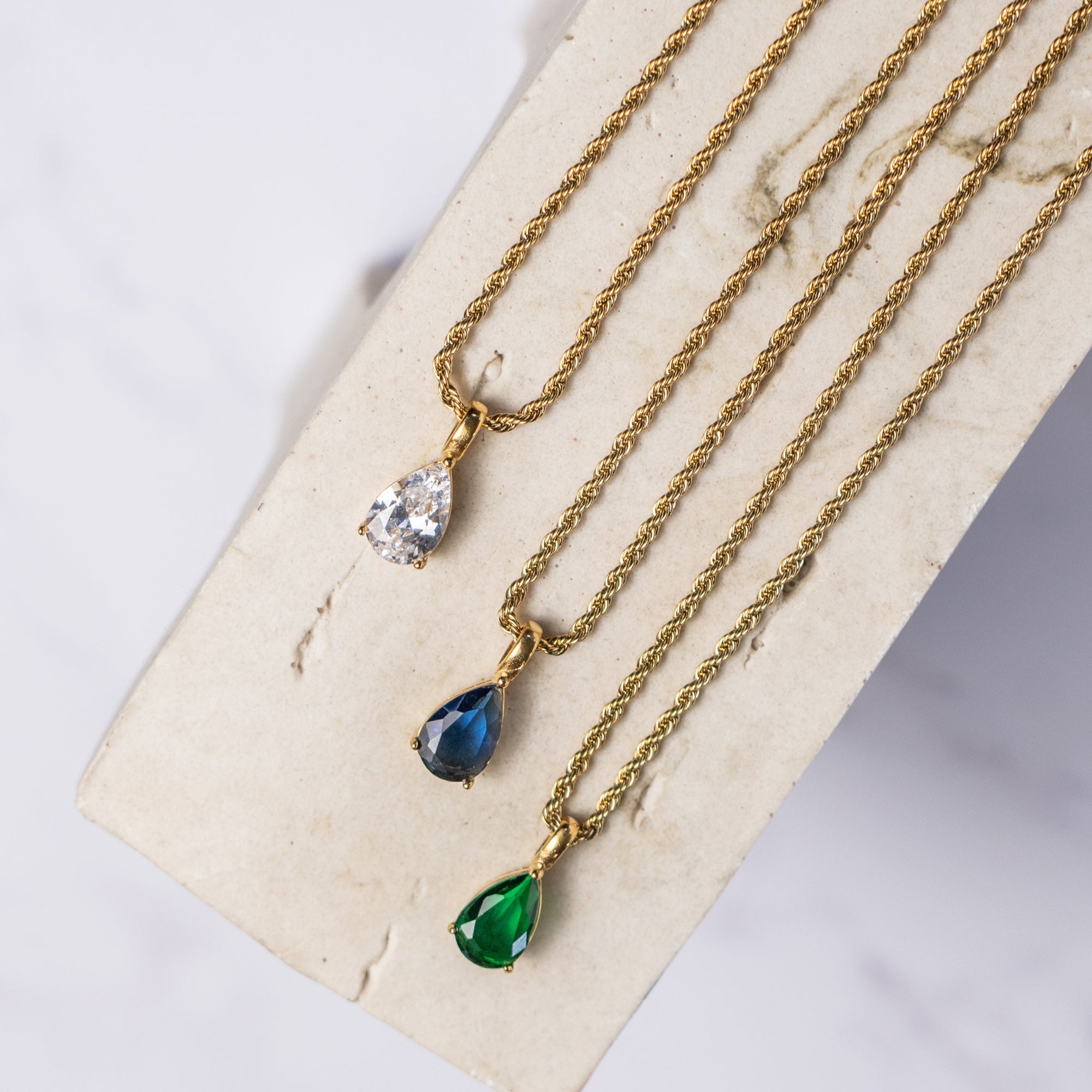 A collection of gold necklaces with different zirconia pendants: cubic, sapphire, and emerald.