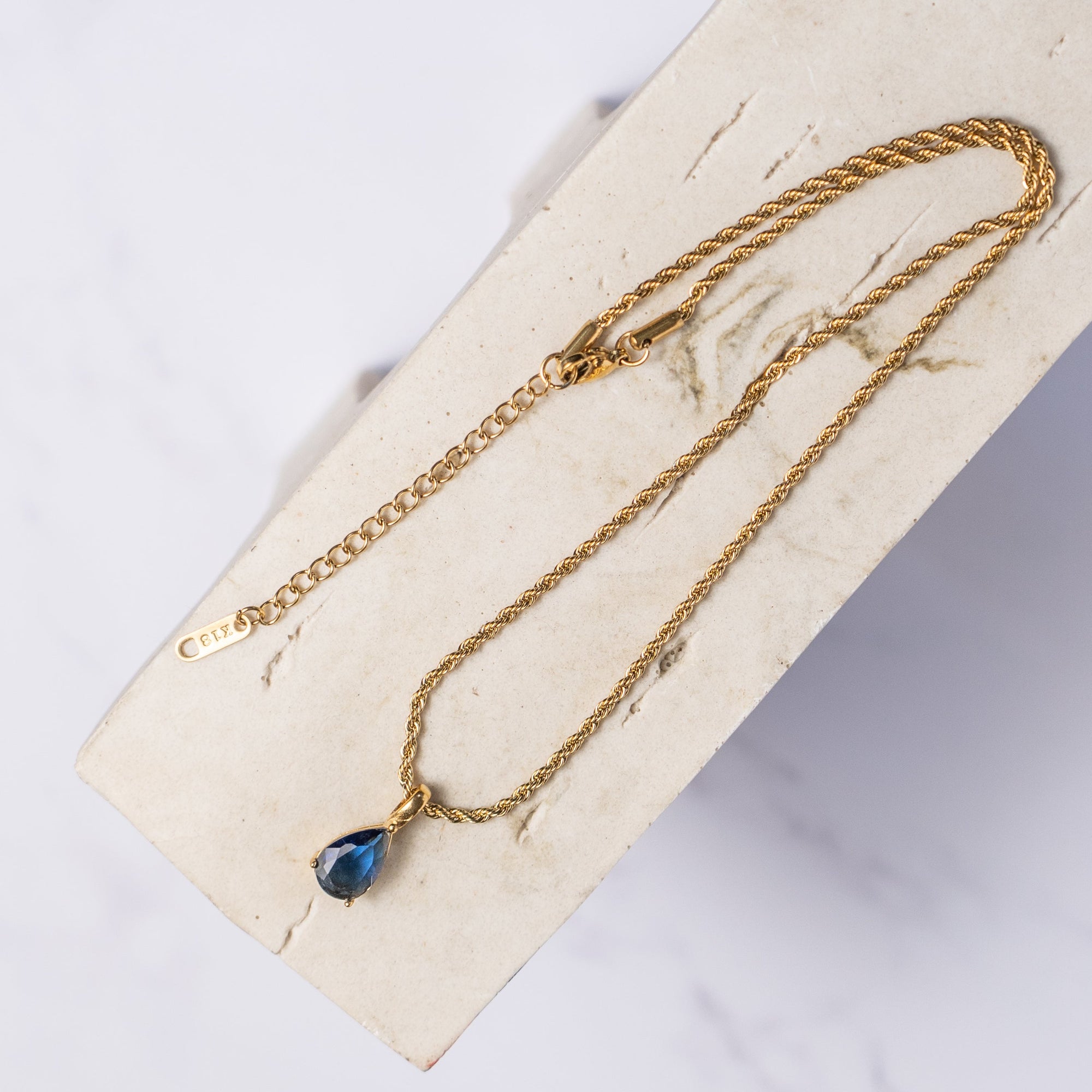 A blue sapphire necklace with a gold chain, displayed on a beige background.