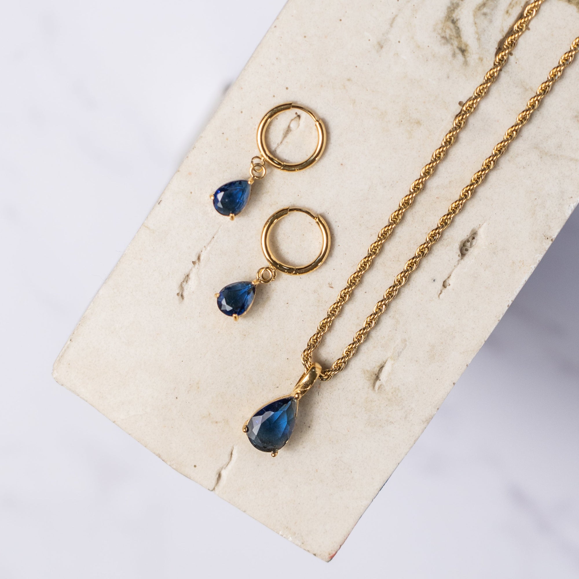 A blue sapphire necklace with a gold chain, displayed on a beige background.