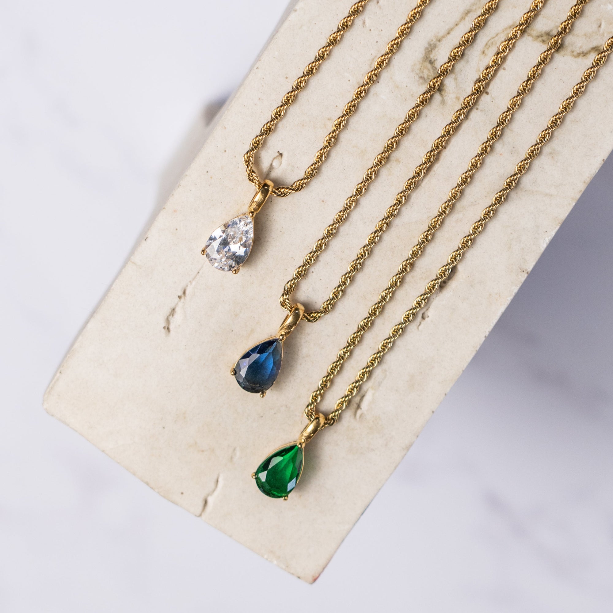 A collection of three gold necklaces with different zirconia pendants: cubic, sapphire, and emerald.