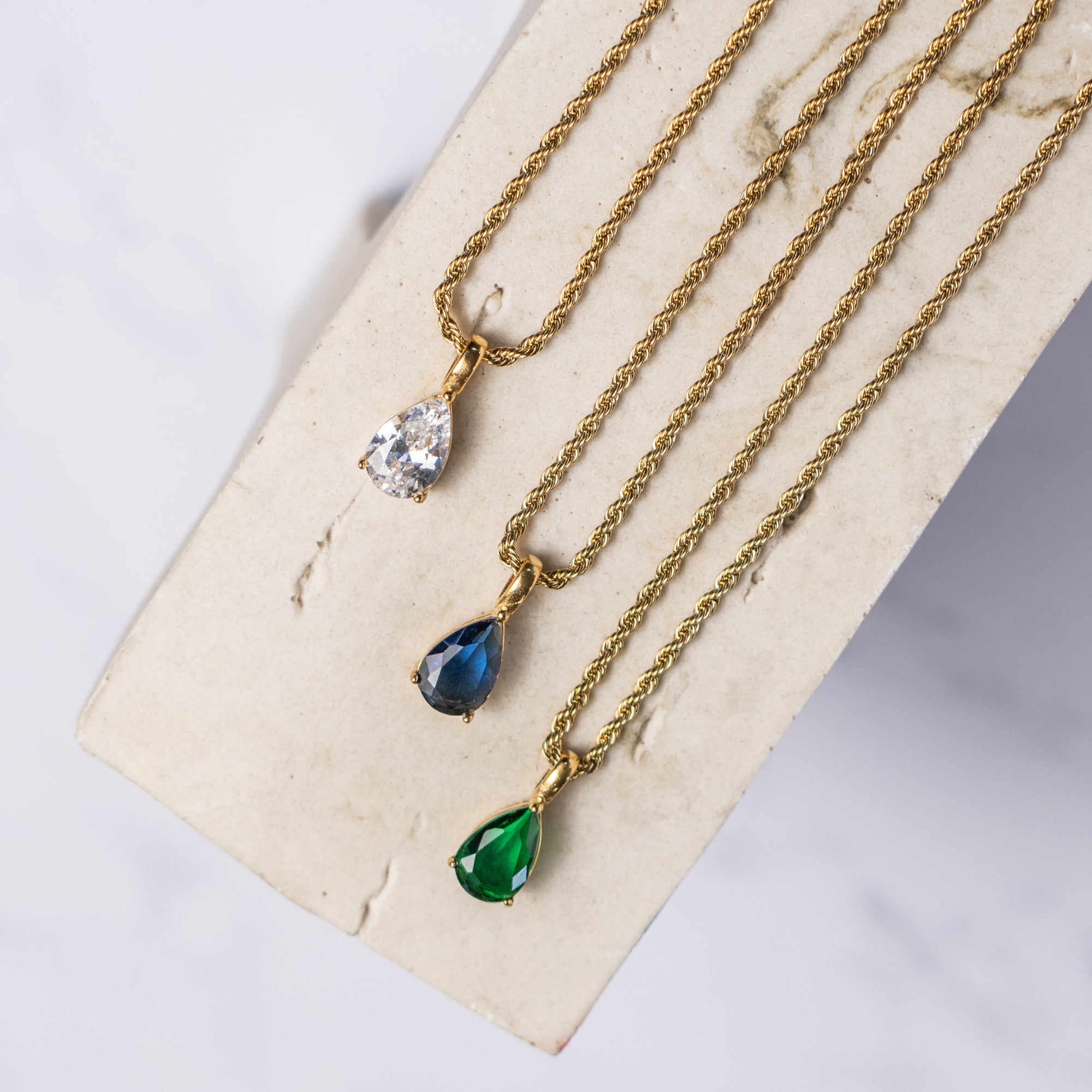 Three gold necklaces with three different pendant colors: clear, sapphire, and emerald.